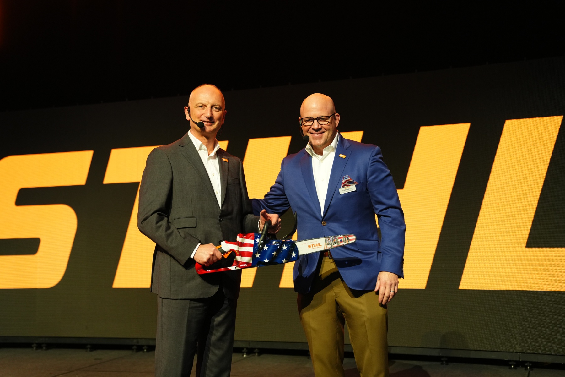 Dr. Nikolas Stihl (t.v.) og Chris Keffer, administrerende direktør for STIHL Inc. i USA, overrekker en jubileumssag med et amerikansk flagg.